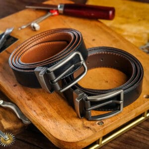 Two black leather belts with silver buckles on a wooden surface.