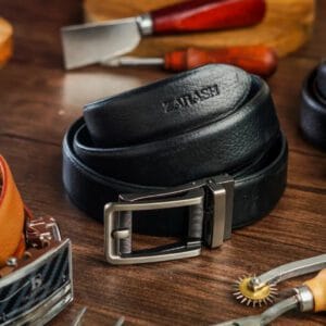 Black leather belt with silver buckle on a wooden surface with tools in the background