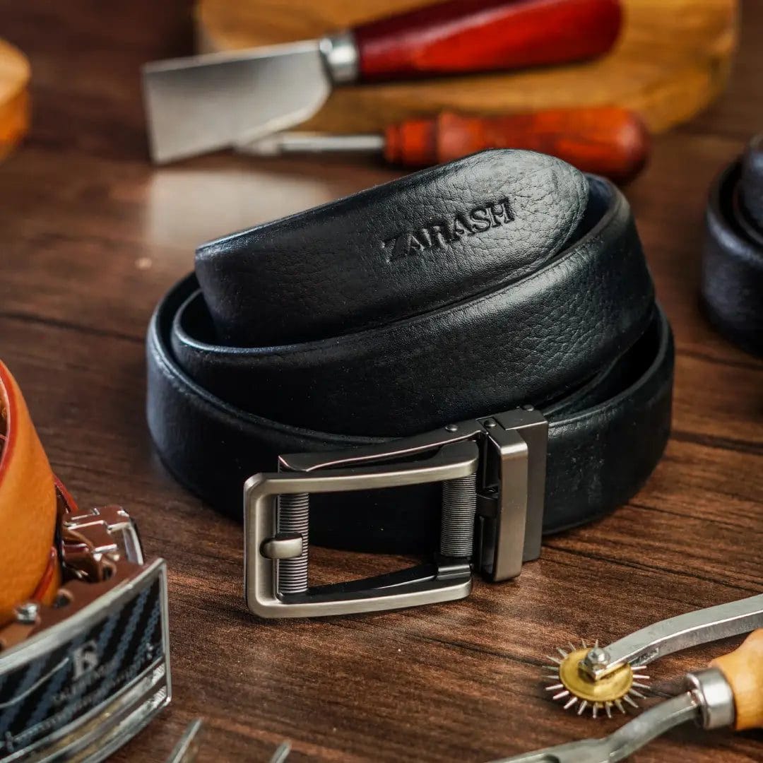 Black leather belt with silver buckle on a wooden surface with tools in the background