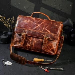 Brown leather satchel bag on a dark surface with tools around